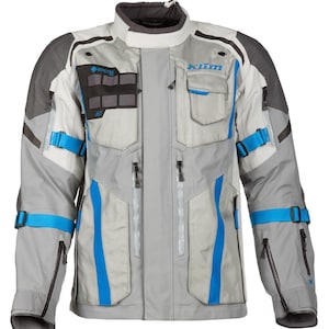 May include: A light grey motorcycle jacket with dark grey shoulder panels, bright blue adjustable straps, and black zips. The jacket features a high collar, multiple pockets, and the word Klim printed in blue on the upper left chest area.