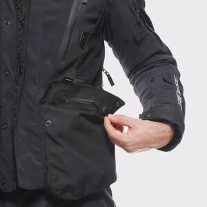 May include: Black motorcycle jacket with multiple pockets and zips. The jacket has a buttoned closure and a mesh panel for ventilation. The sleeve features the brand name in white. The jacket is designed for protection and comfort.