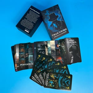 May include: A deck of "True Crime Oracle Cards" with a black box and cards featuring illustrations and text. The box has a silhouette of a fedora-wearing figure. The cards have illustrations and words like "Perversion" and "Mind Control."