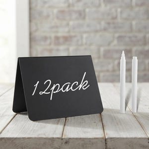 May include: A black tent-style chalkboard sign with the text 12pack written in white cursive script, accompanied by two white liquid chalk markers standing upright. The sign features a smooth matte finish and a folded base for stability.