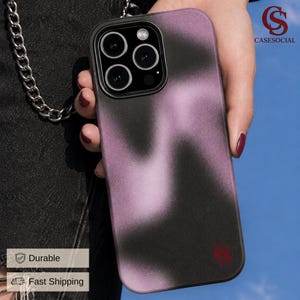 May include: A smartphone case with a black and purple gradient design. The case has a black border and a red logo in the bottom right corner. A silver chain is attached to the phone case.