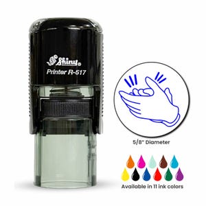 May include: A black Shiny Printer R-517 self-inking stamp with a 5/8 inch diameter circular impression area. The stamp features a blue line art graphic of clapping hands and is available in 11 different ink colors shown as small droplets.
