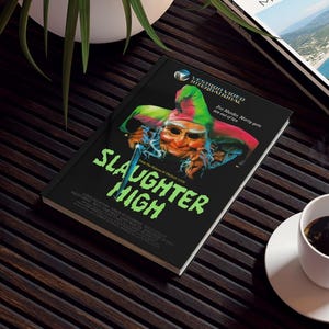 Peut inclure: Une couverture de livre noire avec le titre Slaughter High en grandes lettres vertes. L'illustration montre un personnage de bouffon masqué tenant un couteau. Le texte inclut Vestron Video International, For Murder, Marty gets ten out of ten, et From The Makers Of Friday 13th, ainsi qu'une liste de noms de la distribution et de l'équipe.