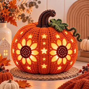 May include: A round, orange crocheted pumpkin featuring intricate cut-out patterns of sunflowers and stars. The pumpkin has a dark brown crocheted stem and a green crocheted leaf with a curly vine. The interior is illuminated with a warm light.