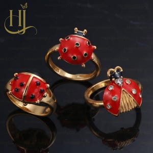 May include: Three gold-toned rings featuring ladybug designs. One ring displays a red ladybug with black spots, another shows a red ladybug with black spots and a black head, and the third features a red ladybug with clear stones and gold wings.