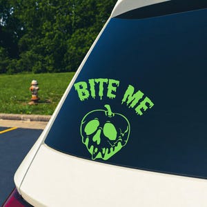 Könnte beinhalten: Ein limettengrüner Vinyl-Aufkleber auf einer Heckscheibe. Der Aufkleber zeigt den Text BITE ME in einer tropfenden Schriftart über einem stilisierten Apfel mit einem totenkopfartigen Kern, der ebenfalls mit einem tropfenden Effekt dargestellt ist.