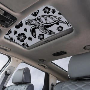 Könnte beinhalten: Ein Auto-Schiebedach mit einem schwarz-weißen Meeresschildkröten-Design, Hibiskusblüten und Blättern auf grauem Hintergrund. Das Schiebedach ist in einem Auto mit grauen Ledersitzen eingebaut.