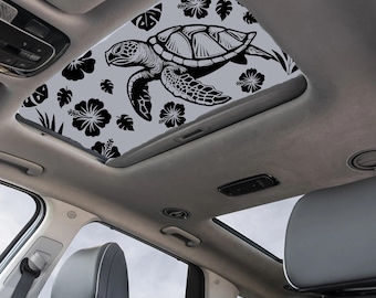 May include: A car sunroof featuring a black and white sea turtle design with hibiscus flowers and leaves on a gray background. The sunroof is installed in a car with gray leather seats.