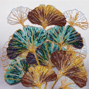 Könnte beinhalten: Ein Perlenstickerei-Kunstwerk auf weißem Stoffhintergrund, das ein Bündel fächerförmiger Ginkgoblätter zeigt. Die Blätter sind detailliert mit kleinen Glasperlen in den Farben Petrol, Dunkelblau, Goldgelb und Metallic-Braun verziert.