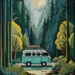 May include: A cross-stitch embroidery depicting a teal and white camper van parked on a path within a dense forest. The scene features tall evergreen trees, yellow-leafed trees, a pale sun, and birds flying in the sky above the van.