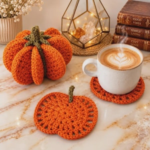 May include: A crocheted orange pumpkin with a green stem, a matching orange pumpkin-shaped crochet coaster, and a white ceramic mug filled with coffee featuring latte art, set near a stack of three books labeled Good Vibes, Simple Living, and Cozy Home.