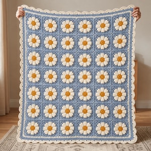 May include: A rectangular crochet blanket featuring a repeating pattern of white daisy motifs with yellow centres on a light blue background. The blanket is finished with a decorative cream-coloured scalloped border along all four edges.