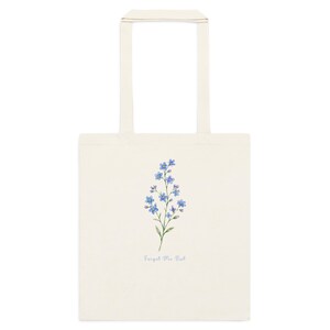 Cream cotton tote bag featuring delicate blue forget me not flowers and “Forget Me Not” text inspired by Outlander and Scottish wildflowers.