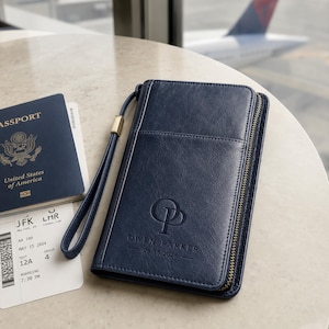May include: A navy blue travel wallet with a wrist strap, featuring the embossed monogram OP, the name OWEN PARKER, and the date 06.15.2026. The wallet has a gold-toned zipper and is positioned next to a United States passport and a boarding pass.