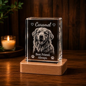 May include: A rectangular clear glass block featuring a laser-etched portrait of a dog. The text "Caramel" is engraved at the top between two hearts, and "Best Friend. Always." is at the bottom with two paw prints. It sits on a wooden base.