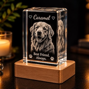 May include: A rectangular clear glass block featuring a laser-etched portrait of a dog. The text reads Caramel, Best Friend. Always. with heart and paw print icons. The glass block is mounted on a rectangular light-colored wooden base.