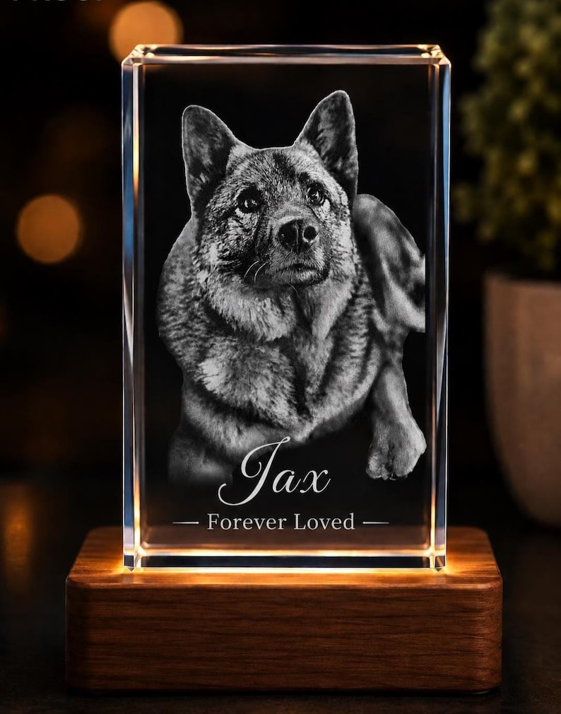 May include: A rectangular clear glass block featuring a laser-etched portrait of a dog. The text "Jax" and "Forever Loved" is engraved below the dog. The glass block rests on a rectangular wooden base that emits a warm light from underneath.
