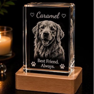 May include: A rectangular glass block featuring a laser-etched portrait of a dog. The text reads "Caramel" between two hearts, and "Best Friend. Always." above two paw prints. The glass block sits on a light-colored wooden rectangular base.
