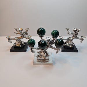 May include: Three decorative stands featuring silver-toned, branch-like structures mounted on square bases. Each stand supports four polished, dark green malachite spheres with distinct banded patterns, arranged in a cluster atop the metal branches.