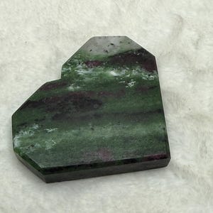 May include: A heart-shaped, polished stone with a mix of green, burgundy, and white colors. The stone has a smooth surface and a geometric shape, with a flat bottom and angled sides.