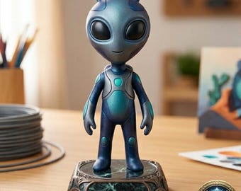 May include: A blue and teal alien figurine with large black eyes and small antennae. The alien is standing on a decorative base with a green marble-like pattern. The figurine is on a wooden surface.