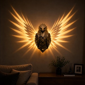 Puede incluir: Aplique de pared con forma de águila de color bronce con alas iluminadas, que proyecta un brillo cálido sobre la pared. La escultura detallada está montada sobre un sofá en un salón. La iluminación crea un efecto dramático.