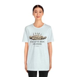 May include: Pale blue t-shirt with a graphic of a person with swords in their back, and the text "COULD'VE BEEN AN EMAIL - 44 BC". The shirt is made of a soft material.