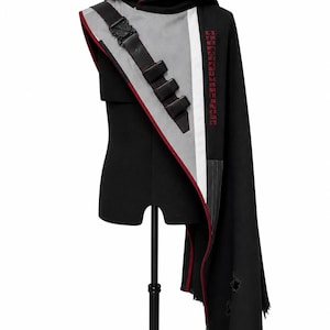 May include: Black hooded cloak with gray and red accents. Features a black strap with buckles and a white stripe. The cloak has a distressed hem and red text on the right side. The hood is lined with red fabric.