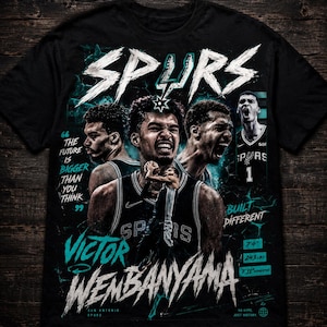 Pode incluir: Camiseta preta com um design gráfico com a palavra "SPURS" em branco e o nome "VICTOR WEMBANYAMA" em branco e turquesa. A camiseta inclui imagens de jogadores de basquete e o texto "BUILT DIFFERENT".