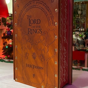 May include: A leather-bound book with gold accents and the title "The Lord of the Rings" by J.R.R. Tolkien. The book is closed and has a decorative design on the front cover.