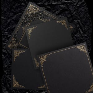 May include: Black square cards with gold ornate corner designs and borders. One card features a detailed gold floral frame. The cards are arranged on a dark, textured surface, creating a contrast between the gold and black.