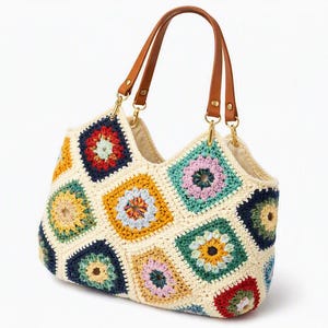 May include: A crochet handbag featuring a multi-colored granny square pattern in shades of navy blue, mustard yellow, light pink, and teal, all joined by cream-colored yarn. The bag includes two brown leather handles attached with gold-tone metal hardware.