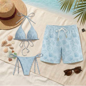 May include: A light blue bikini and matching swim trunks set with a seashell pattern. The bikini top is halter-style, and the bottoms are tie-side. The swim trunks have a drawstring waist. A straw hat and sunglasses are also present.