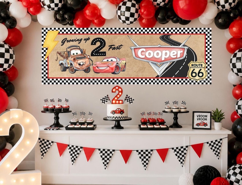 May include: A rectangular banner featuring a checkered border, a yellow lightning bolt, and the text Growing up 2 Fast. It displays cartoon cars, a road, and a Route 66 sign with the name Cooper. The banner is set against a wall with balloons.