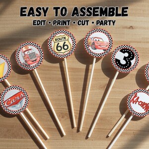 May include: A set of circular cupcake toppers on white sticks featuring racing-themed graphics including a Route 66 sign, a red race car, the number 3, a lightning bolt, and the text Cars and KA-CHOW. The text EASY TO ASSEMBLE EDIT PRINT CUT PARTY is visible.