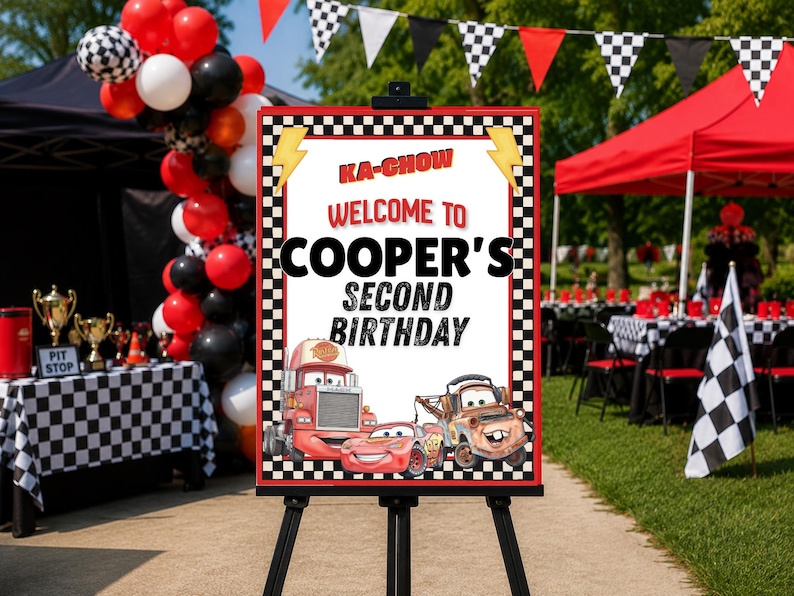 Puede incluir: Un letrero de cumplea&ntilde;os rectangular sobre un caballete negro con un borde a cuadros, rayos amarillos y el texto KA-CHOW WELCOME TO COOPER'S SECOND BIRTHDAY. El letrero muestra ilustraciones de tres coches de carreras de dibujos en rojo y marr&oacute;n.