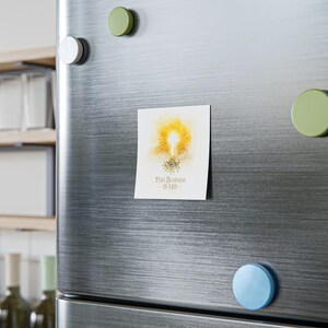 Può includere: Un magnete bianco con un disegno ad acquerello di un sole giallo e piccoli accenti floreali. Il testo "This Business Is His" è stampato in oro. Il magnete è attaccato alla porta di un frigorifero in acciaio inossidabile.
