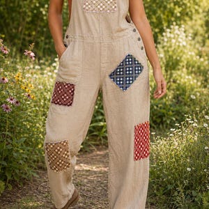 May include: Beige overalls featuring a square bib pocket and four scattered patches in red, blue, and brown plaid patterns. The garment has adjustable shoulder straps with metal buckles, side buttons, and deep pockets on the legs and hips.