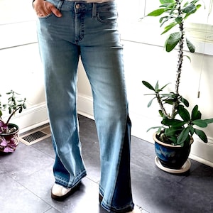 Könnte beinhalten: Hellblaue Jeans mit zweifarbigem Design. Die Jeans hat ein weites Bein und einen kontrastierenden dunkelblauen Einsatz an der Außenseite jedes Beins. Die Jeans wird mit weißen Schuhen getragen.