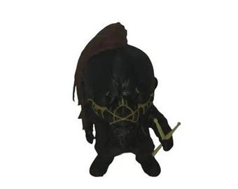 May include: A black figurine with a hood and a stylized face, featuring yellow accents. The figure is holding two yellow drumsticks. The hood is a dark maroon color. The figurine has a unique, artistic design.