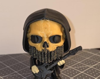 May include: A 3D-printed figurine of a skeletal figure in a black hooded robe, holding a black guitar. The skull is tan with black eye sockets and a beard. The figurine is on a gray surface.