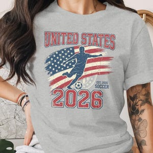 Gray t-shirt with United States Soccer 2026 graphic and American flag.