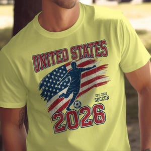 Yellow t-shirt with distressed American flag, soccer player, and "UNITED STATES SOCCER EST. 2026" text.