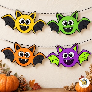 May include: A decorative banner featuring four cartoon bat cutouts in yellow, green, orange, and purple, each with black wings, large white eyes, and two small fangs. The bats are strung together on a black and white twisted cord for display.