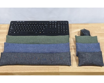 May include: A set of three rectangular keyboard wrist rests and three matching rectangular mouse wrist rests in olive green, blue, and charcoal gray fabric. The wrist rests are positioned in front of a black computer keyboard and a black computer mouse.