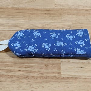 May include: A rectangular quilted oven mitt in a vibrant blue fabric featuring a repeating pattern of small light blue flowers. The mitt includes a white fabric loop attached to one end for hanging, providing a functional design for kitchen use.