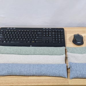 May include: A black keyboard and mouse set with three rectangular wrist rests in shades of green, white, and blue. The keyboard is positioned above the wrist rests on a wooden surface.