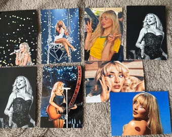 Puede incluir: Colección de ocho postales con una mujer rubia en varias poses. Algunas tarjetas son en blanco y negro, otras en color. Las imágenes incluyen a la mujer cantando, tocando la guitarra y posando con signos de paz.
