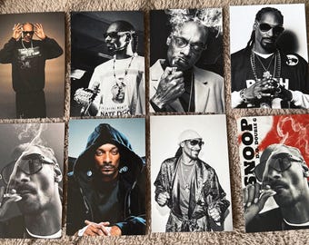 Puede incluir: Una colección de ocho impresiones de retratos de Snoop Dogg en varias poses. Las imágenes son principalmente en blanco y negro, con algunos acentos de color. Snoop se ve usando gafas de sol, joyas y varios atuendos, con algunas imágenes que lo muestran fumando.