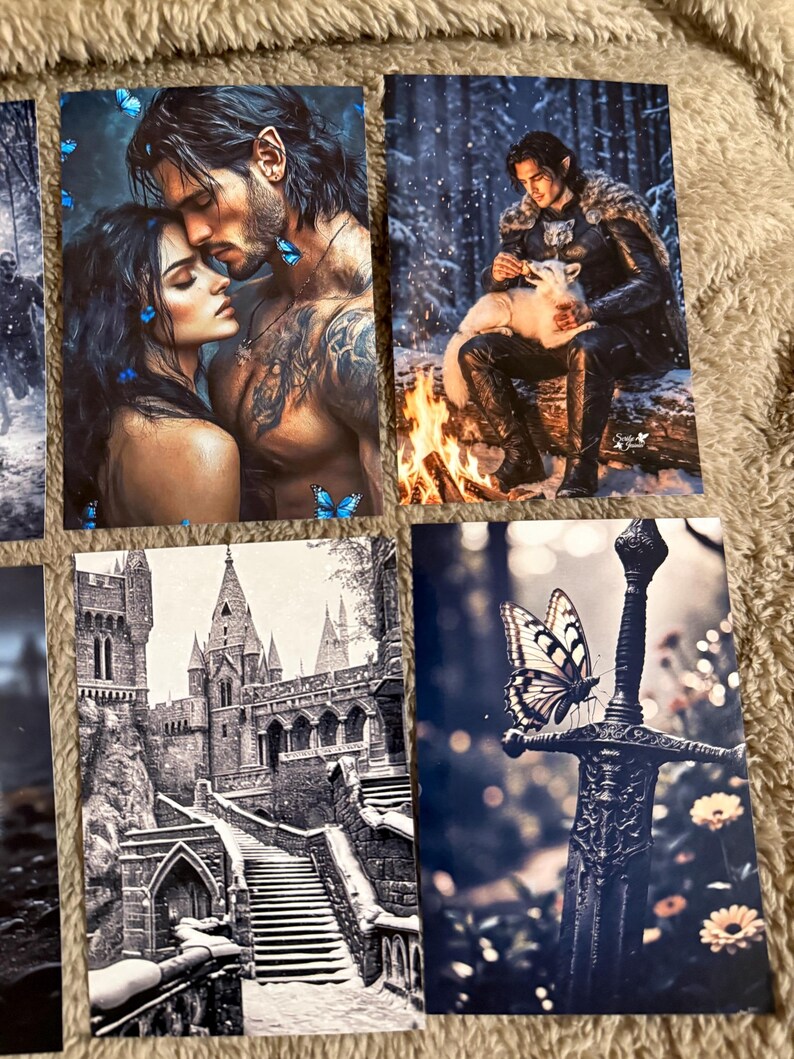 May include: A collection of fantasy art prints featuring romantic couples, a figure with a white fox by a fire, a castle, and a sword with a butterfly. The prints have a dark, moody aesthetic with detailed illustrations.